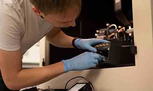 Man in blue gloves inserting item into black equipment